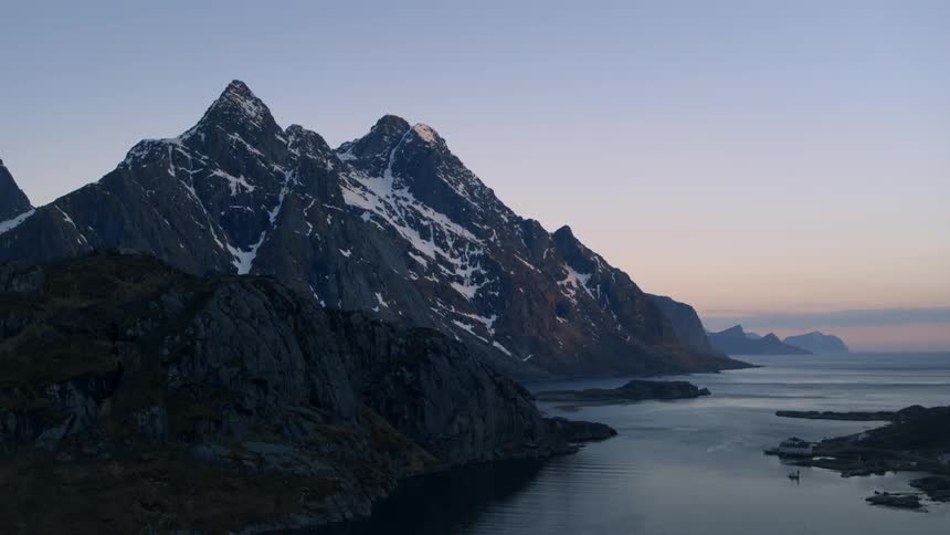 Dusk is settling over a mountains dotted with snow on the coast