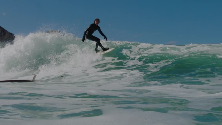 A surfer avoids another surfer as he rides a wave off a remote coastline