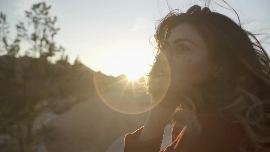 A woman smiles as the wind blows her hair as she stands in the desert at sunset