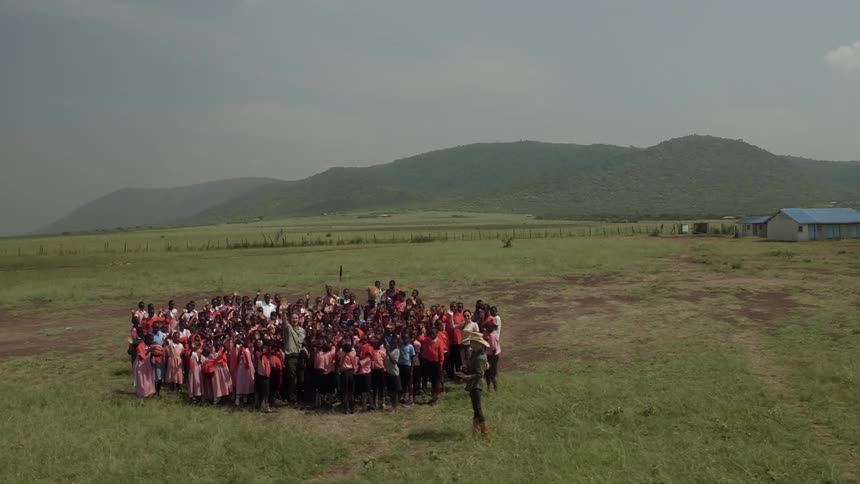 A group of school children gather in a field and clap