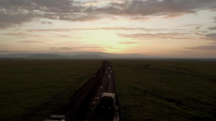 Two trucks travel on a dirt road