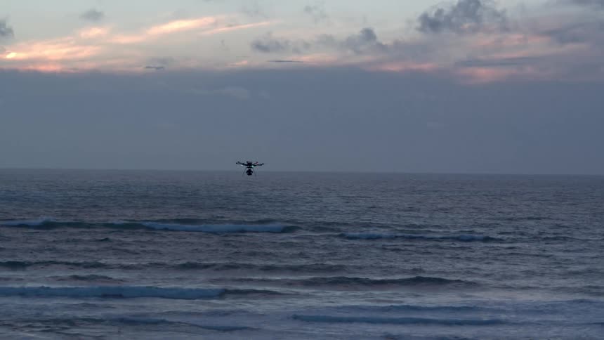 A drone is flying over the water at sunset