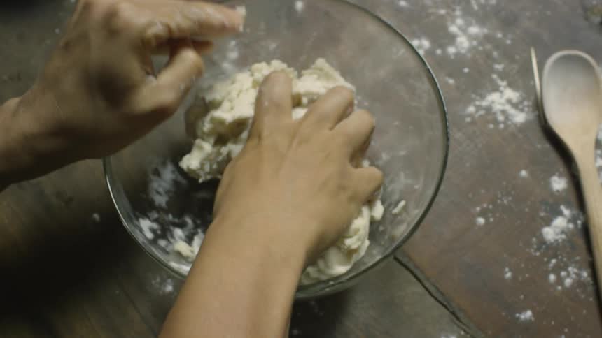 A person mixes dough with their hands in a bowl