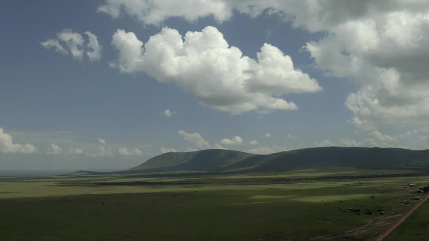 Clouds hover over a verdant plain and hills during the day