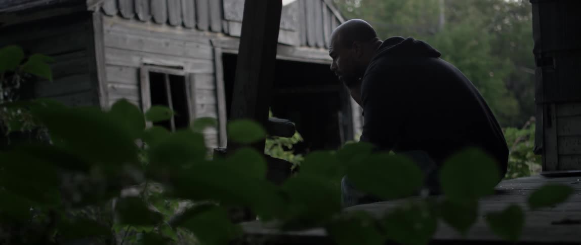 A man is sitting in a yard leaning forward