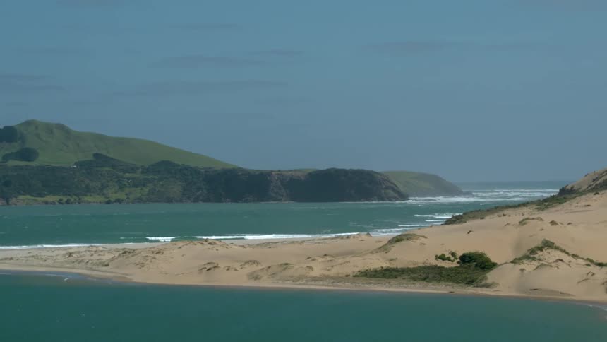 Waves roll onto the shore of a beach and inlet during the day