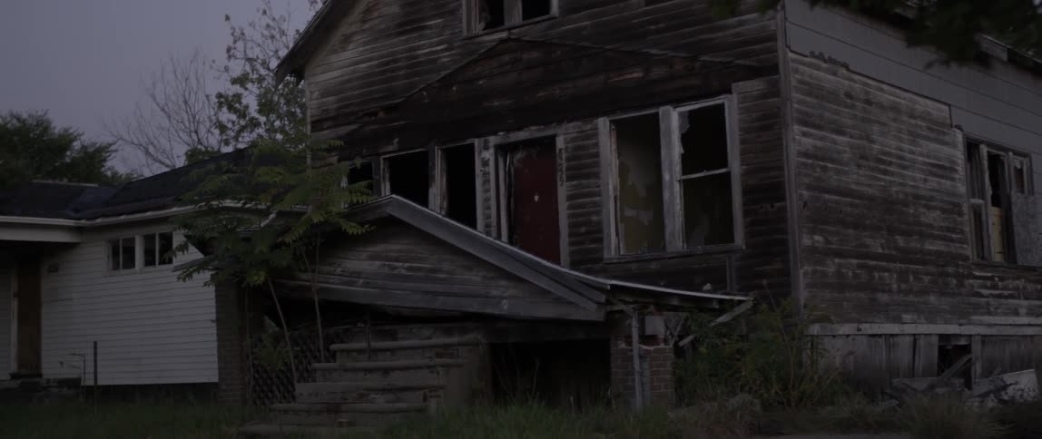 An old residential building needing renovation sits beneath a large tree at dusk