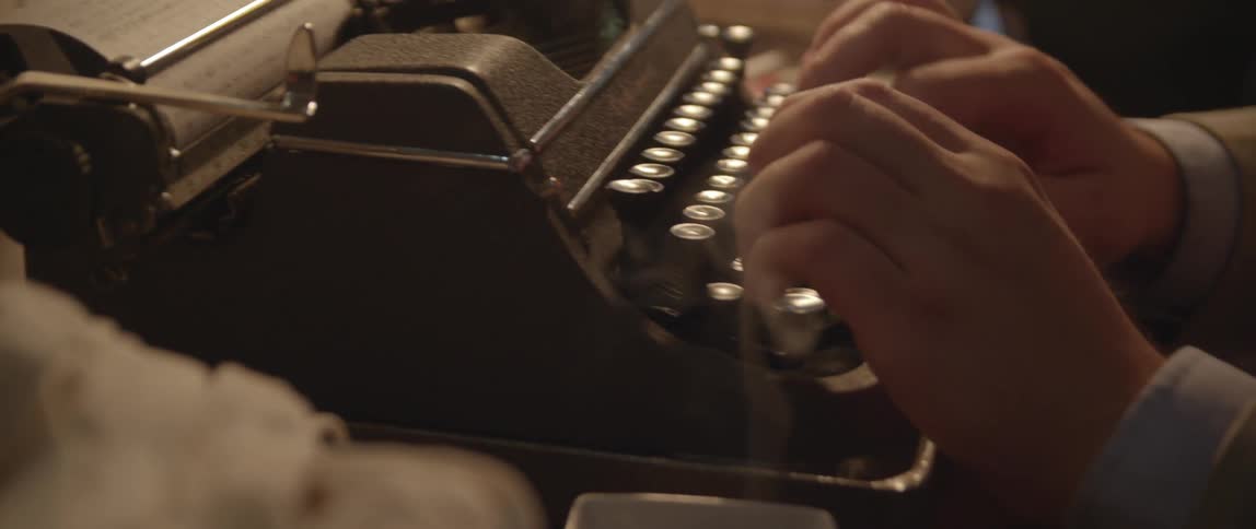 Cigarette smoke rises up from the ashtray as a male types on an old vintage typewriter
