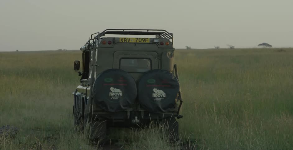 Two jeeps travel on a dirt path across an african savanna during the day