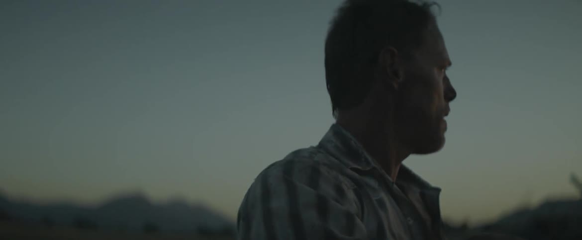 A man leans on a shovel and breathes heavily outside at dusk