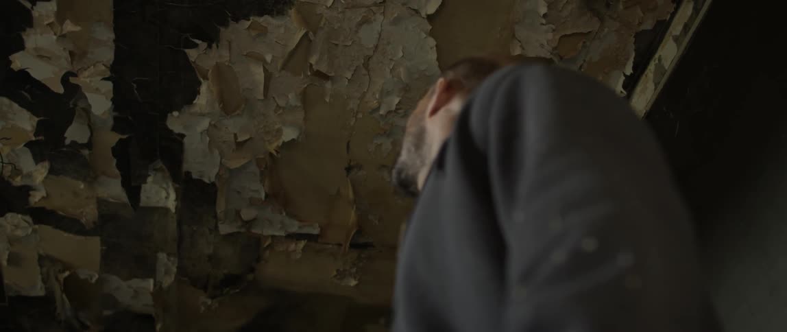 Man standing and looking around in a tattered building with a decaying ceiling