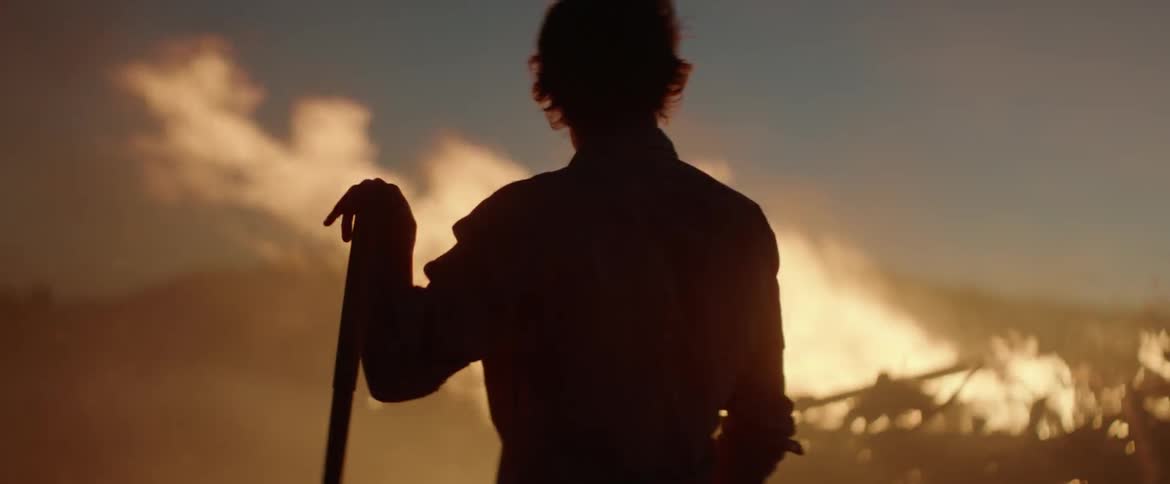 A man is holding a shovel by a large fire in the field