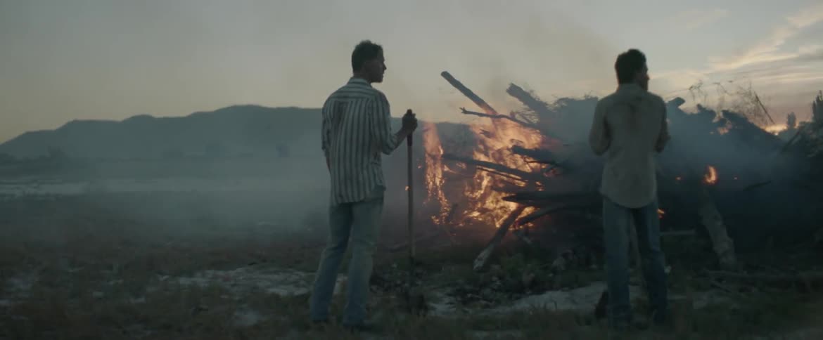 Two men watch a fire burn