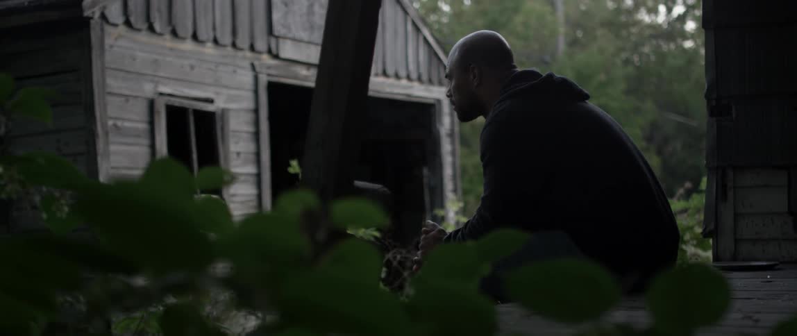 A man is sitting down leaning forward towards a barn