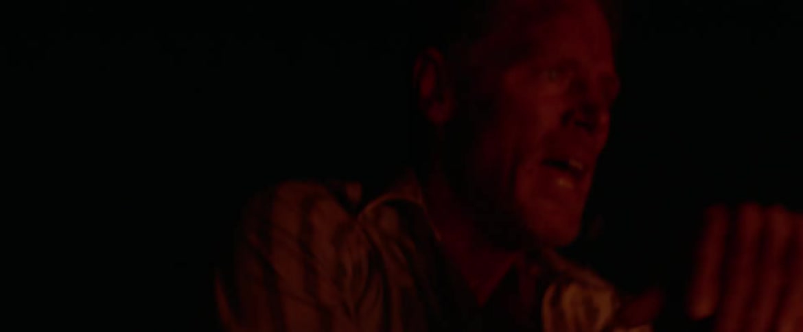 A man battling a fire at night breathes heavy as he stops to wipe his brow