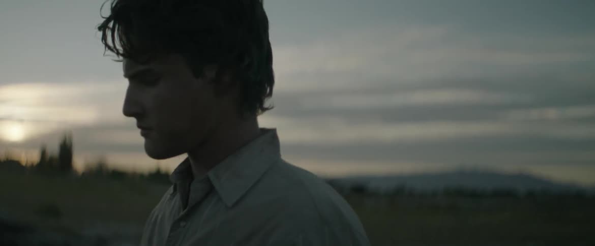 The wind blows a man's hair as he stands looking up toward the sky at dawn
