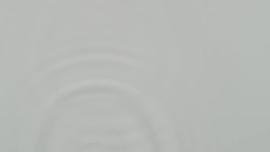 Drops of liquid fall causing ripples to spread across the surface of the water