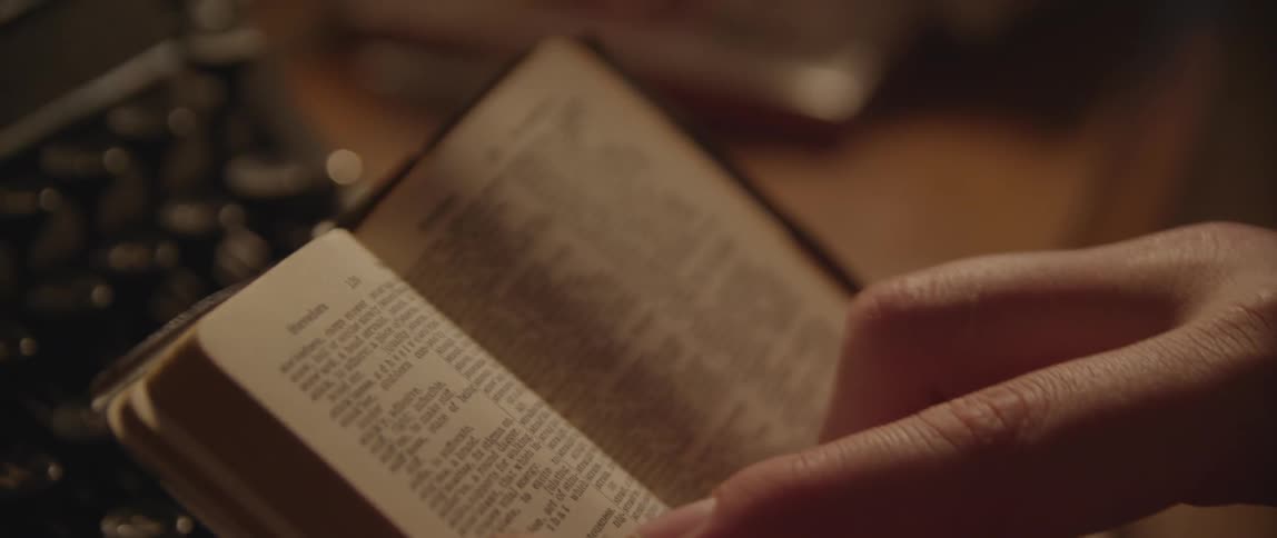 Closeup of hands holding a small book with a typewriter in the background