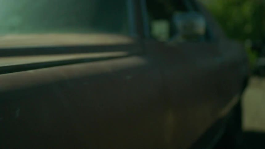 A car with rusted panels sits in the sunshine