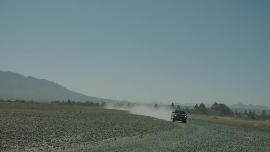 Racing along the dirt track the red suv speeds by icing up a huge cloud of dust