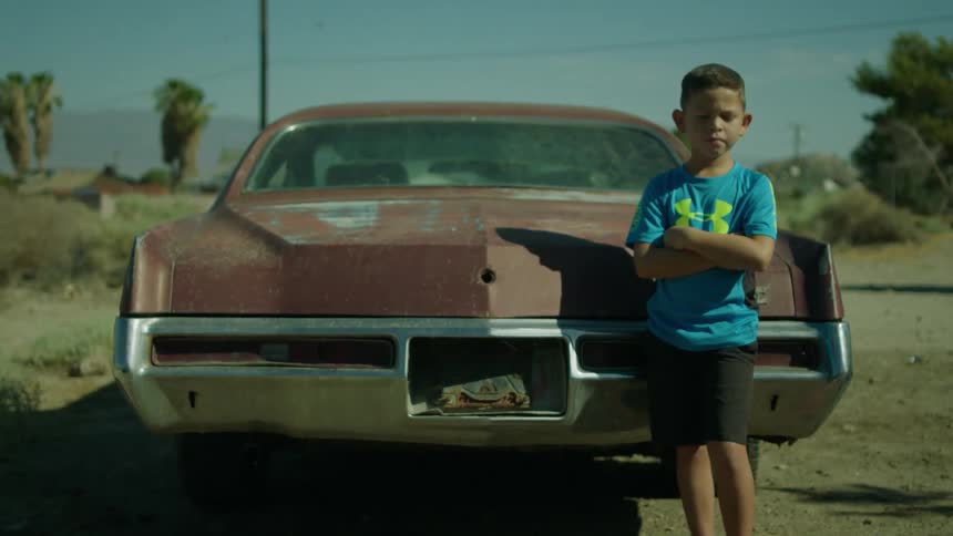 A young boy leans against a rusty car