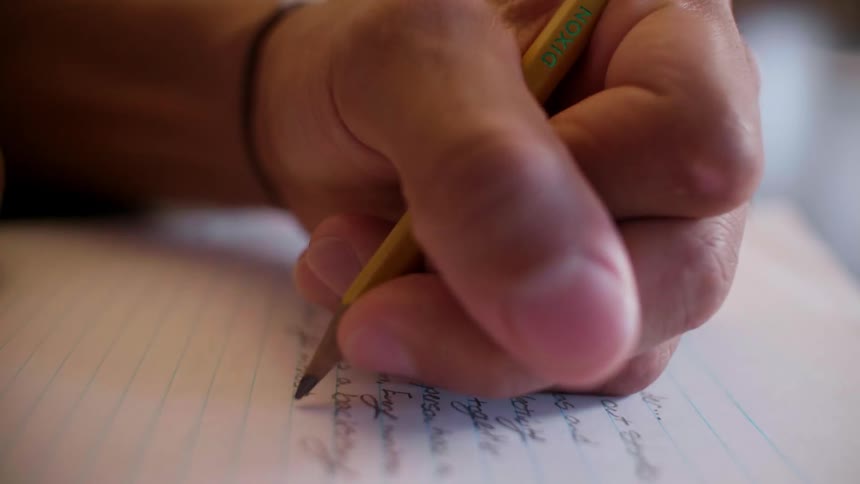Man writes in a notebook using a pencil