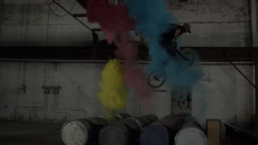 A man does a large jump over barrels in a warehouse