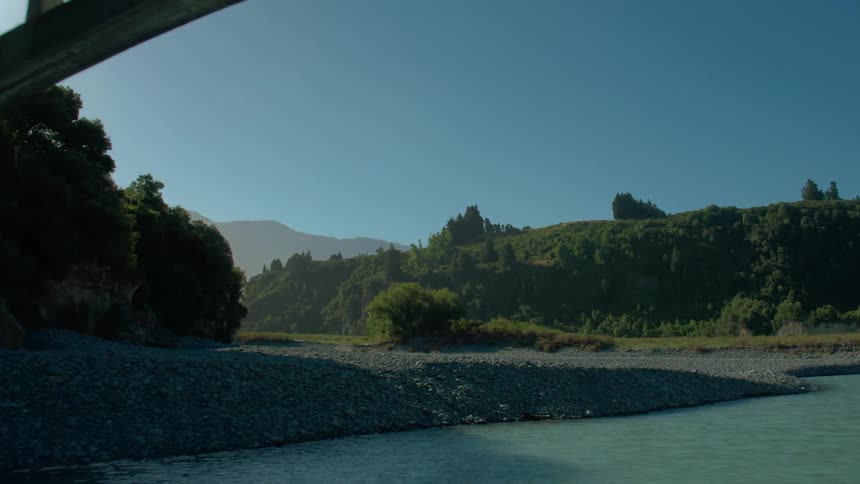 Moving aerial view going under a bridge of a river and then over some lad on a clear day