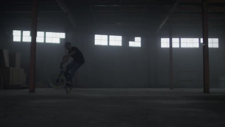 A man riding a bike in a warehouse is doing tricks on it