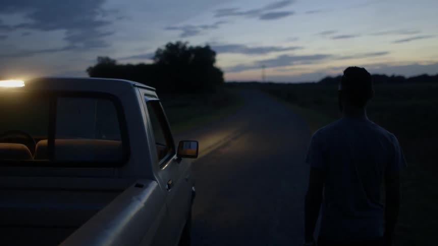 A man stands outside a pickup truck at dusk