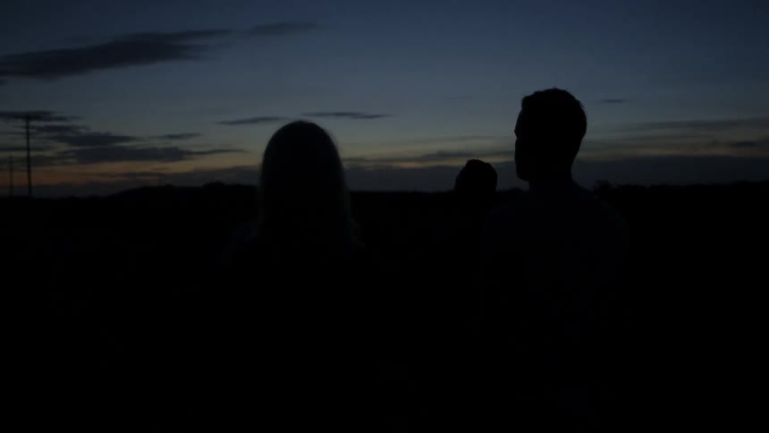 4 people are standing on the side of a dark road at dusk