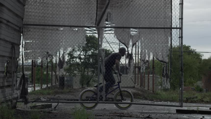 Man rides small bike near a chain link fence