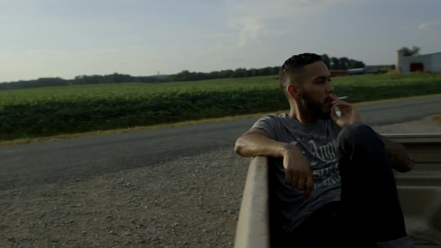 A man is sitting in the back of a pickup smoking