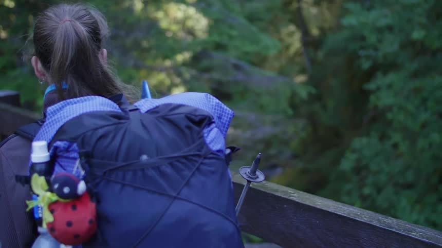A woman wearing a backpack walks over a bridge