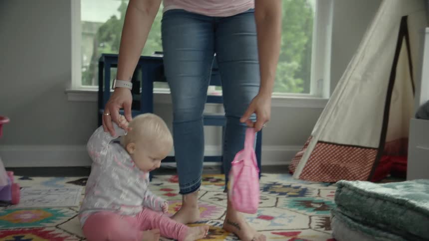A woman helps a baby walk to the middle of the room