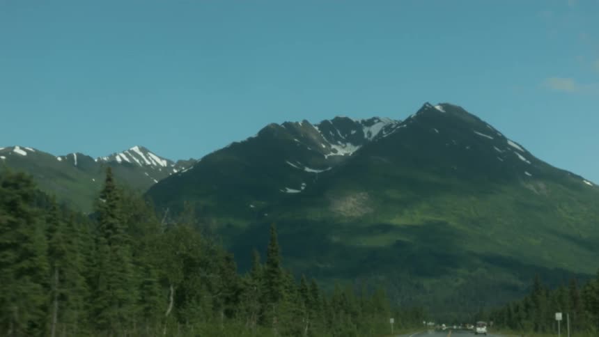 Vehicles travel on a two lane road in a mountain setting during the day