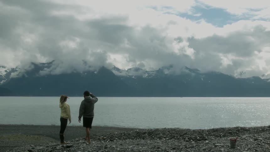 A man jogs up and throws a rock into a lake