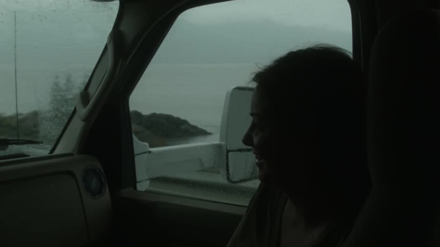 A female passenger in a vehicle is smiling and laughing during a drive
