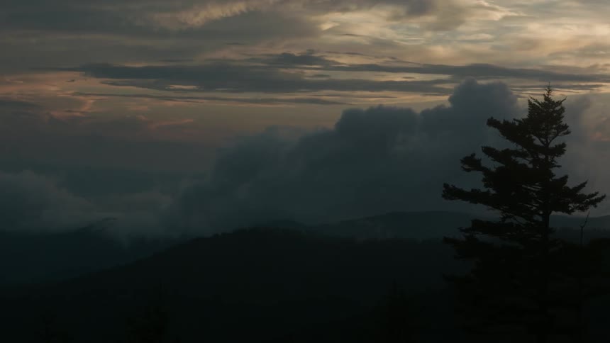 Storm clouds rise over a mountain landscape at dusk