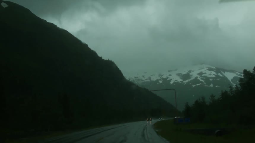 Cars drive on mountain road during rainstorm