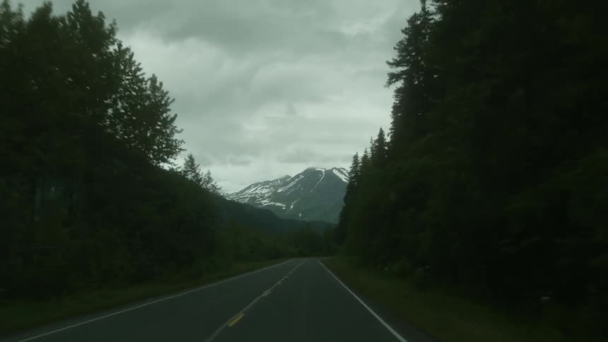Dense forest surrounds a road with a huge mountain ahead