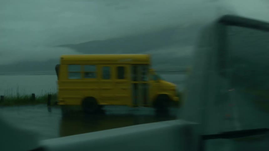 A small school bus in pulled over on a rainy road