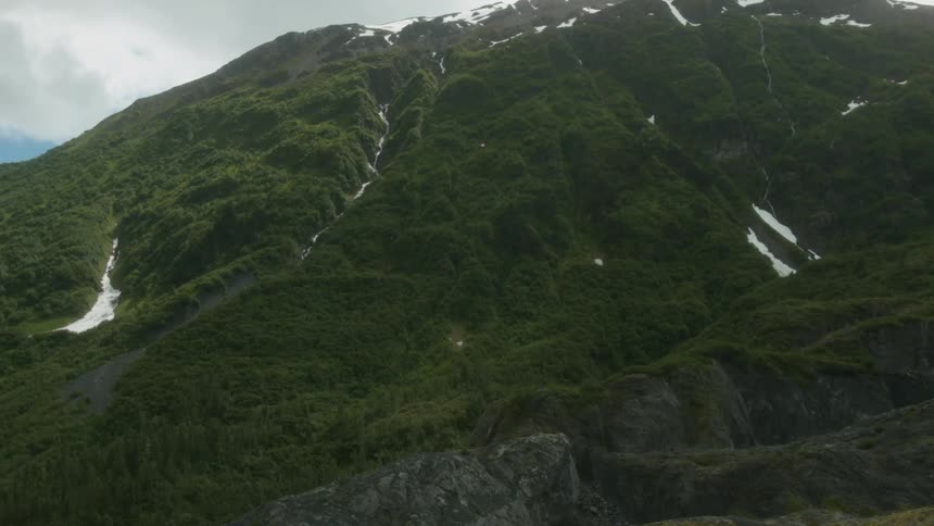 Snow clings to the crevices and peaks of a mountain during the day
