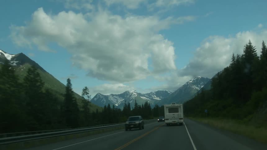An rv travels down a wooded road toward mountains