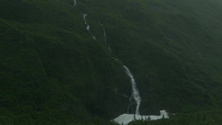 A waterfall cascades down a rolling hillside into a river