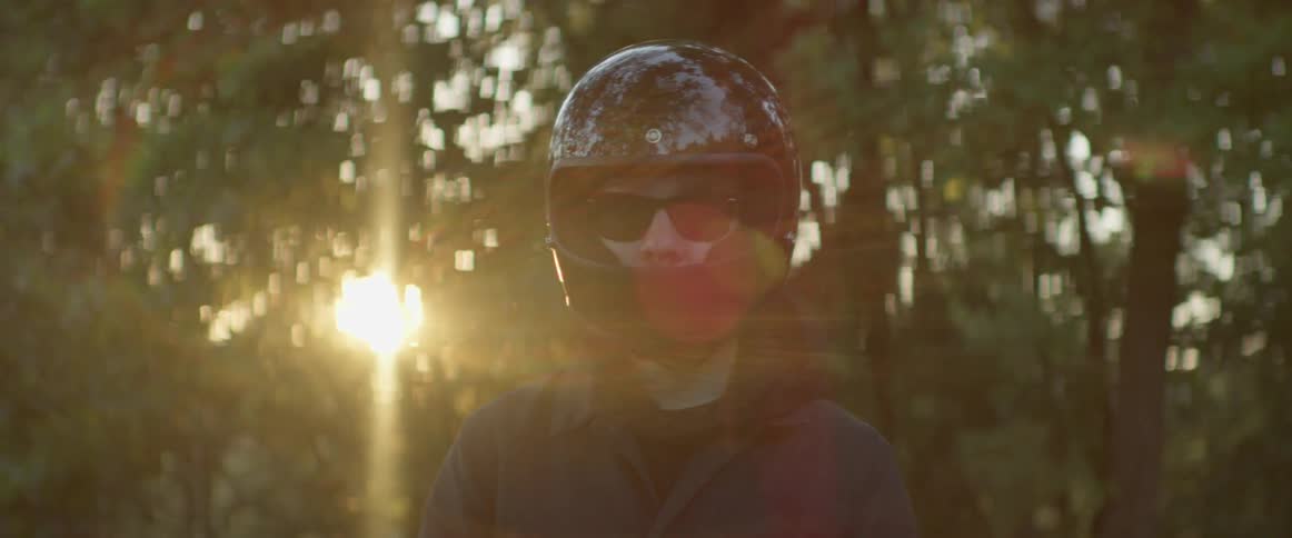A man is wearing sunglasses and a bike helmet with the sun over his shoulder