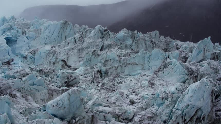 Snow falls in the air around a glacier during the day