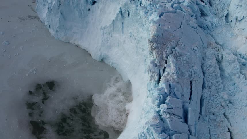 Snow and ice calves off a glacier and splashes in the ocean
