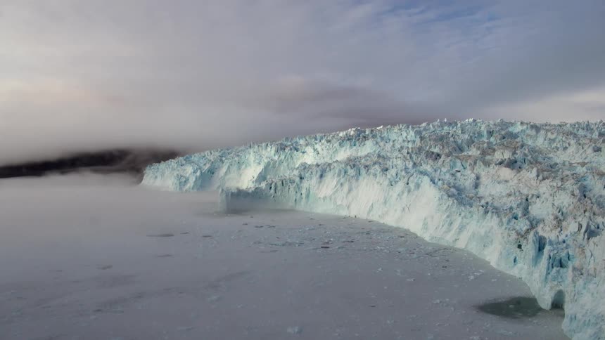 Fog hangs over a coastline dominated by a glacier on a stormy day