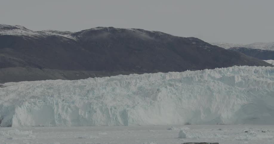 Icebergs float in the ocean at the base of a glacier during the day